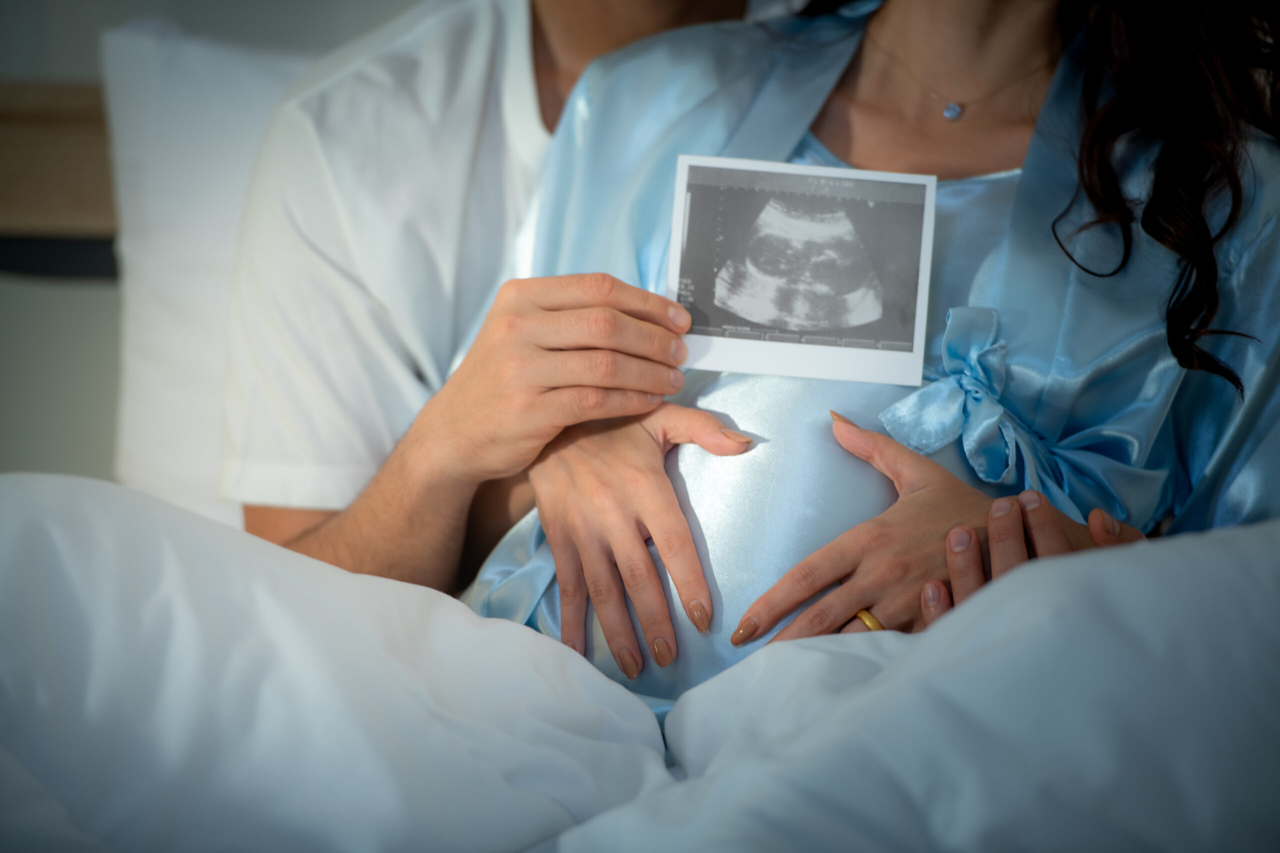 Couple holding an ultrasound scan while embracing the baby bump.